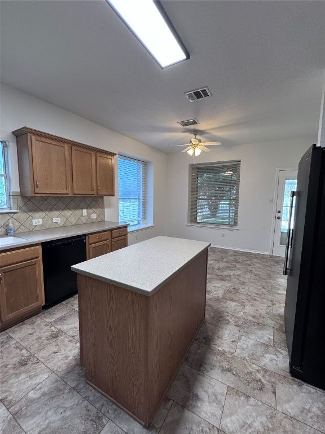 Kitchen featuring black dishwasher, freestanding refrigerator, light countertops, backsplash, and plenty of natural light | Image 7