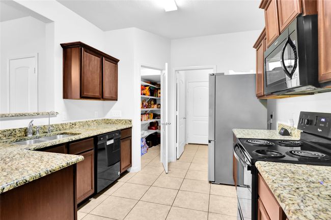 Kitchen with a sink, black appliances, light stone counters, and light tile patterned flooring | Image 12