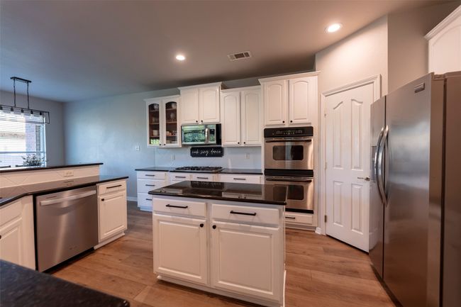 Kitchen featuring appliances with stainless steel finishes, white cabinetry, glass insert cabinets, backsplash, and light wood-style flooring | Image 13
