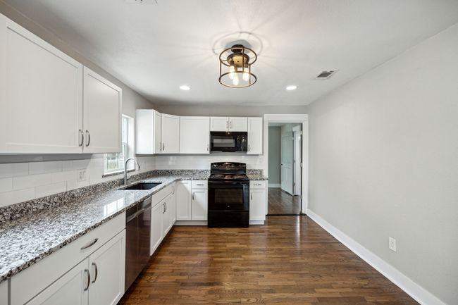 Kitchen with white cabinetry, black appliances, light stone countertops, dark wood-type flooring, and recessed lighting | Image 9