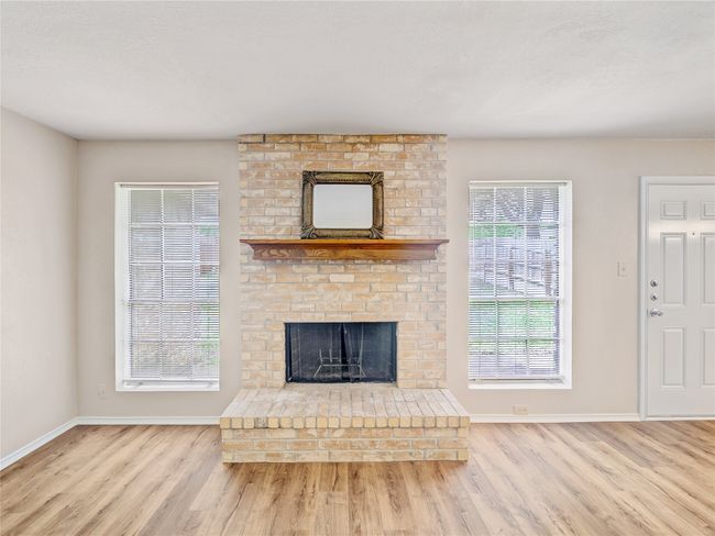 Unfurnished living room featuring wood finished floors, baseboards, and a brick fireplace | Image 6