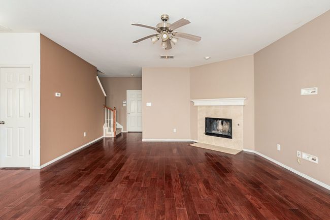 Unfurnished living room with ceiling fan, wood finished floors, stairs, and a fireplace | Image 10