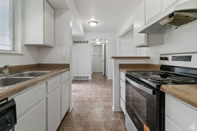 Kitchen with electric range, under cabinet range hood, white cabinets, and dark countertops | Image 4