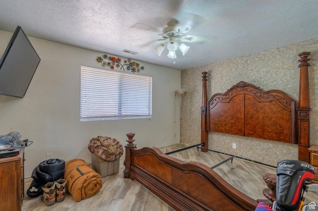Bedroom with wood finished floors, a textured ceiling, ceiling fan, and wallpapered walls | Image 32