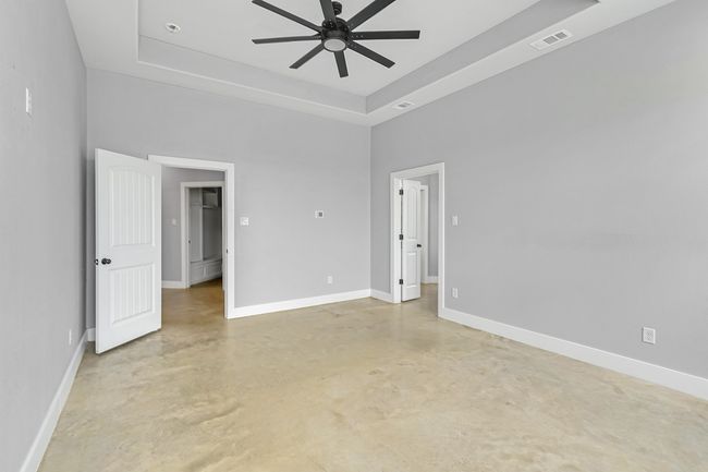 Empty room with concrete flooring, ceiling fan, a tray ceiling, baseboards, and a high ceiling | Image 28
