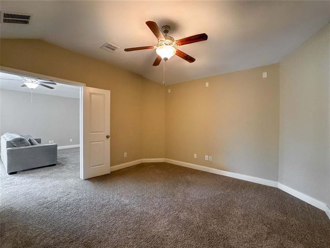 This room features a neutral color palette with carpeted flooring, a ceiling fan, and ample natural light. It connects to another room, offering flexibility for use as a bedroom or office space. | Image 33