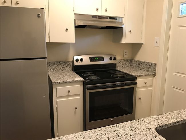 Kitchen with under cabinet range hood, white cabinets, light stone countertops, and appliances with stainless steel finishes | Image 13