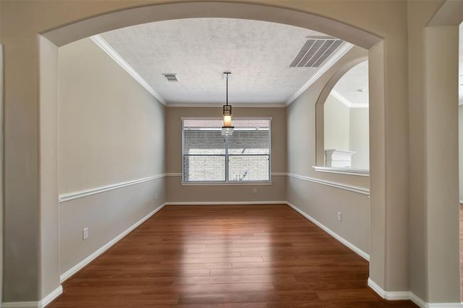 This is a cozy dining area with warm wood flooring, neutral walls, and a modern pendant light. An arched opening connects it to an adjacent room, enhancing the open feel. A large window provides natural light, creating a welcoming atmosphere. | Image 10