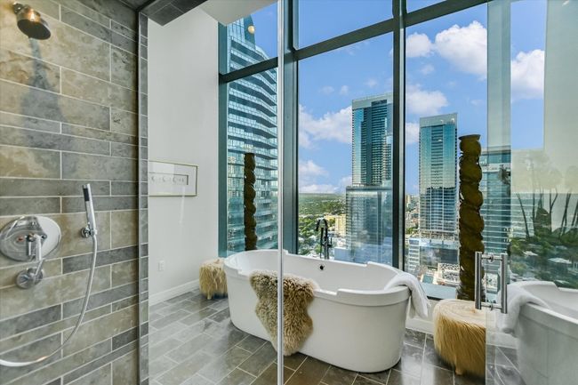 The oversized glass shower features multiple shower heads and sleek tilework for a luxurious experience. | Image 24