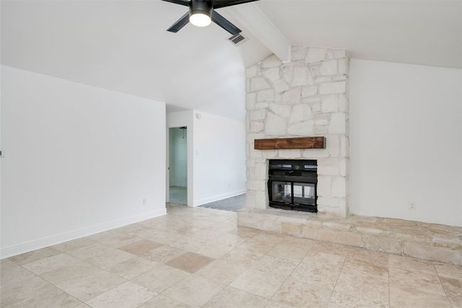 Unfurnished living room featuring a ceiling fan, a stone fireplace, lofted ceiling with beams, and visible vents | Image 9