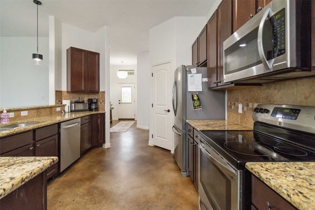 Kitchen with stainless steel appliances, concrete floors, tasteful backsplash, light stone counters, and dark brown cabinetry | Image 12