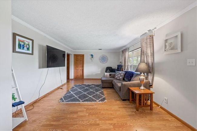 Living area featuring a textured ceiling, ornamental molding, baseboards, and light wood-style floors | Image 15
