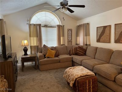 Living room with a textured ceiling, lofted ceiling, ceiling fan, and dark colored carpet | Image 2