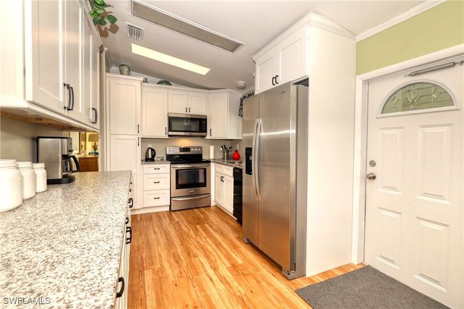 Kitchen featuring stainless steel appliances, white cabinetry, lofted ceiling, and light hardwood / wood-style floors | Image 6