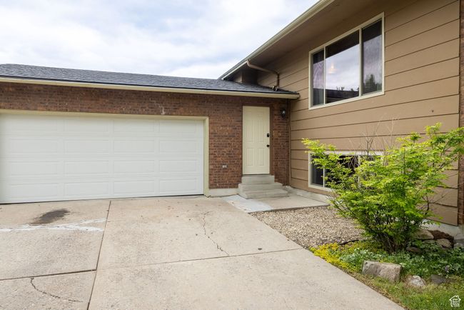 Property entrance with driveway, brick siding, a garage, and a shingled roof | Image 4