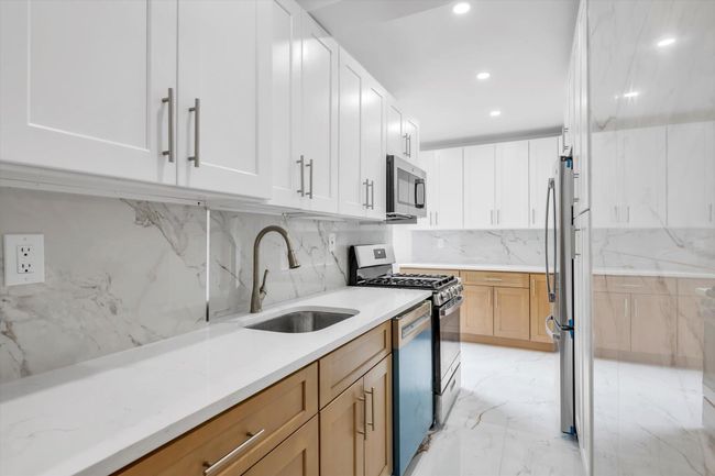 Kitchen featuring appliances with stainless steel finishes, recessed lighting, backsplash, light marble finish flooring, and white cabinetry | Image 7