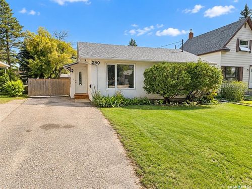 White exterior with dark-shingle roofing, featuring a front lawn, mature shrubs, and a gravel driveway | Card Image
