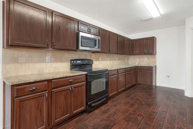 Kitchen with black range with electric stovetop, stainless steel microwave, dark wood-style floors, decorative backsplash, and baseboards | Image 17