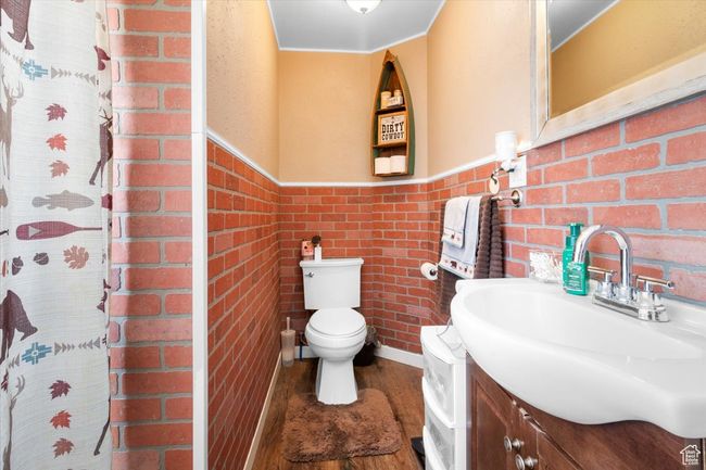 Full bath with toilet, wood finished floors, vanity, brick wall, and wainscoting | Image 37