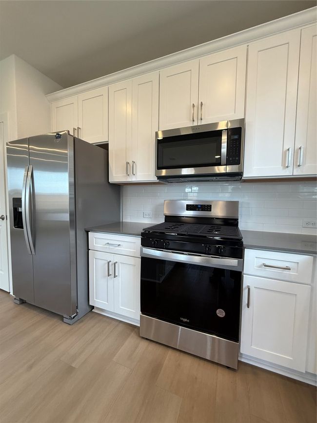 Kitchen with range, fridge, light wood finished floors, white cabinets, and decorative backsplash | Image 18