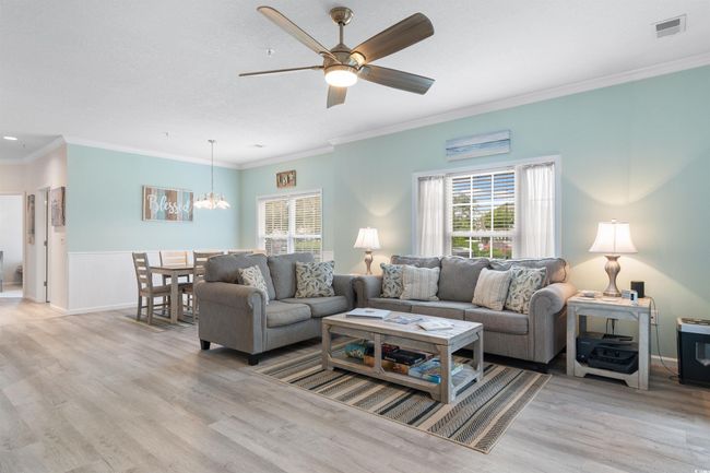 Living room featuring a chandelier, healthy amount of natural light, light wood finished floors, crown molding, and a wainscoted wall | Image 12