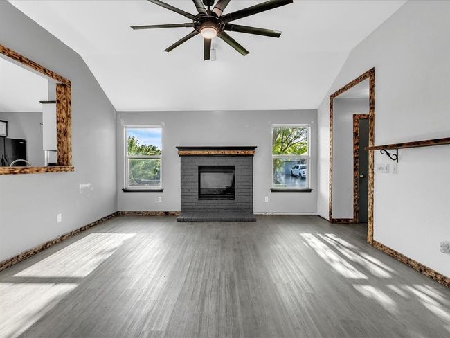 Unfurnished living room featuring wood finished floors, vaulted ceiling, ceiling fan, a fireplace, and baseboards | Image 4