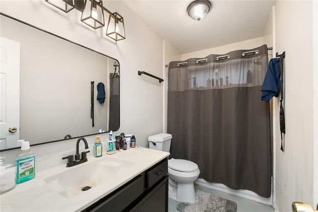 The secondary bathroom features a tub/shower combo, sleek black cabinetry with white counters, and a framed mirror—well-lit and ready for use. | Image 16
