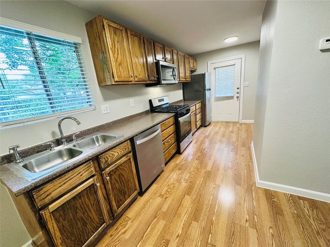 Kitchen featuring appliances with stainless steel finishes, light wood-style flooring, dark countertops, and brown cabinetry | Image 5