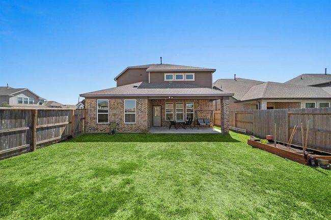 This photo shows the backyard of a two-story brick house with a covered patio, neatly fenced yard, and well-maintained lawn, ideal for outdoor activities and entertaining. | Image 21