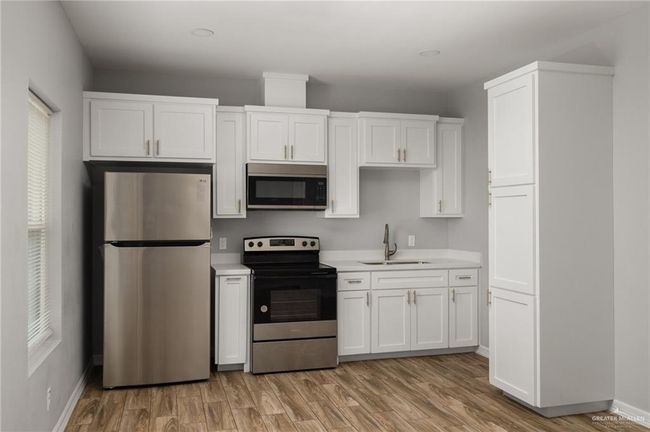Kitchen with stainless steel appliances, light countertops, white cabinets, a sink, and light wood-type flooring | Image 5
