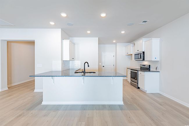 Kitchen with a kitchen bar, a sink, dark stone countertops, stainless steel appliances, and a peninsula | Image 24