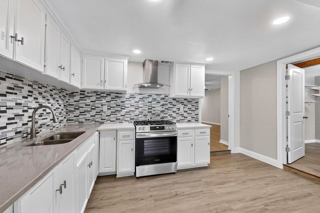 Kitchen featuring stainless steel gas stove, wall chimney exhaust hood, light wood-style flooring, white cabinets, and recessed lighting | Image 28