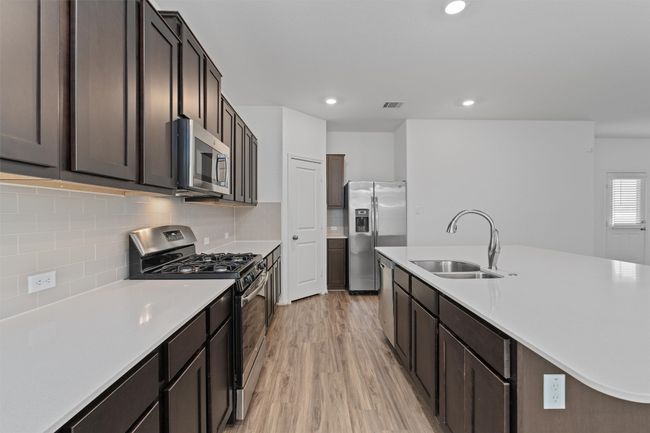 Kitchen featuring stainless steel appliances, tasteful backsplash, light countertops, light wood-style flooring, and a sink | Image 7