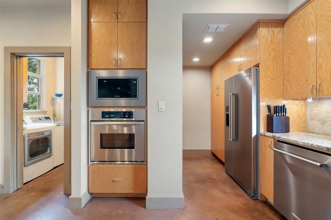 Kitchen with appliances with stainless steel finishes, finished concrete floors, independent washer and dryer, decorative backsplash, and light stone counters | Image 15