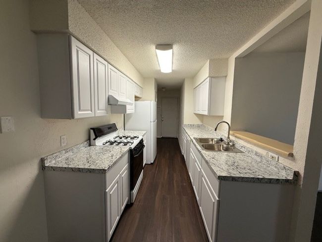 Kitchen with gas range, a sink, under cabinet range hood, light countertops, and a textured ceiling | Image 4