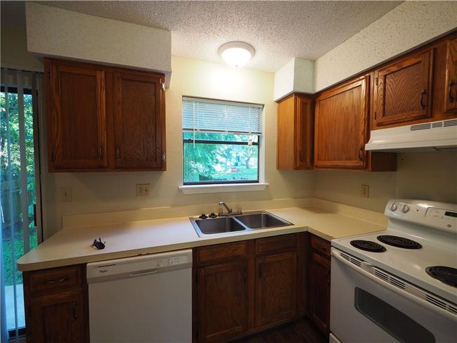 Kitchen with white appliances, under cabinet range hood, a sink, a textured ceiling, and light countertops | Image 7