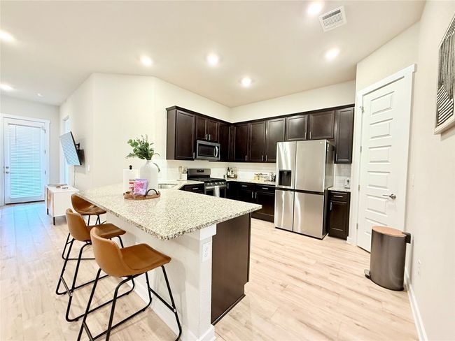 Kitchen with a peninsula, a breakfast bar, appliances with stainless steel finishes, visible vents, and light wood-style floors | Image 6