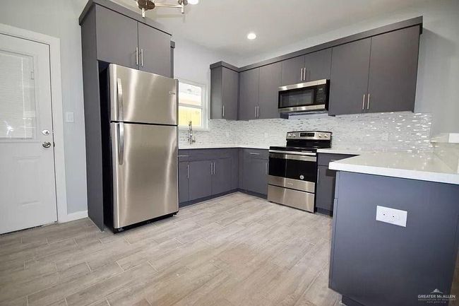 Kitchen featuring stainless steel appliances, light wood-style flooring, gray cabinetry, and decorative backsplash | Image 6