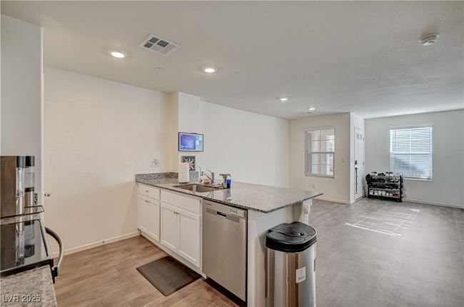 Kitchen with stainless steel dishwasher, electric range, a peninsula, light stone counters, and white cabinets | Image 11