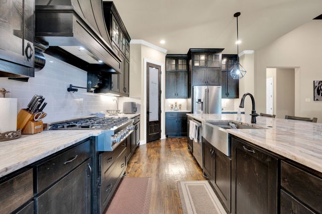 Kitchen featuring custom exhaust hood, stainless steel appliances, glass insert cabinets, dark wood-style floors, and tasteful backsplash | Image 11