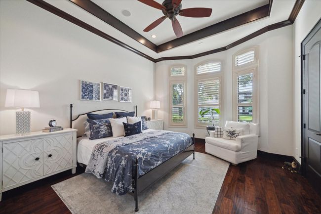 Each of the bedrooms is secluded in its own wing of the house and this charming secondary bedroom is bright and inviting, with a curved wall of windows dressed in plantation shutters that flood the space with natural light. Creamy white walls and trim are punctuated with handsome millwork and dark hardwood flooring, creating an elegant contrast. An ensuite bathroom, walk in closet and serene palette make this room feel both stylish and functional—perfect for guests or family alike. | Image 33