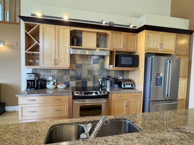 Kitchen with appliances with stainless steel finishes, open shelves, light brown cabinetry, and dark stone countertops | Image 6