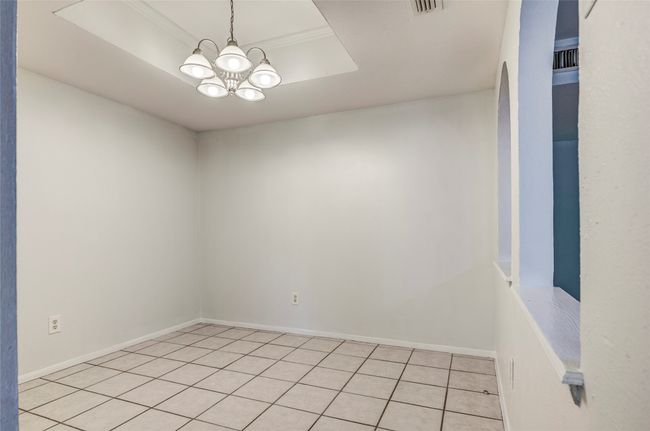 Empty room with a chandelier, light tile patterned flooring, a raised ceiling, and baseboards | Image 14