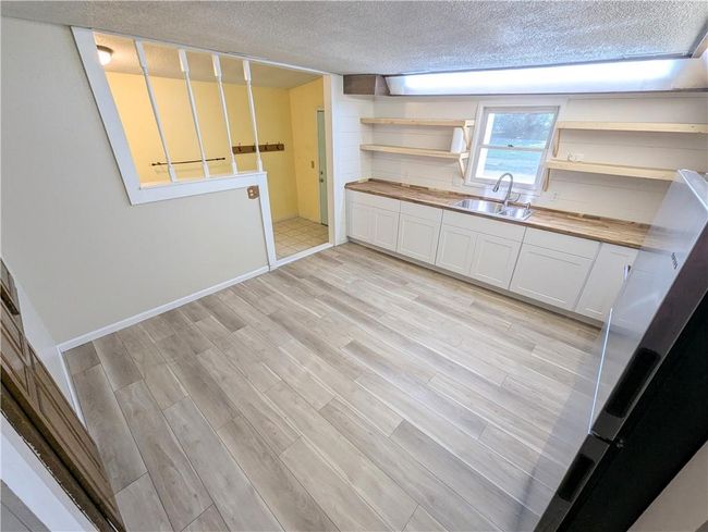 Kitchen with open shelves, a sink, a textured ceiling, butcher block counters, and light wood finished floors | Image 23