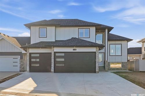 Contemporary two-story exterior with light-colored siding, black-framed windows, stone accents, and a two-car garage with modern doors | Card Image