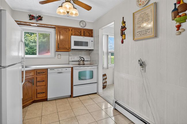 Kitchen featuring white appliances, brown cabinetry, light countertops, ornamental molding, and light tile patterned floors | Image 5