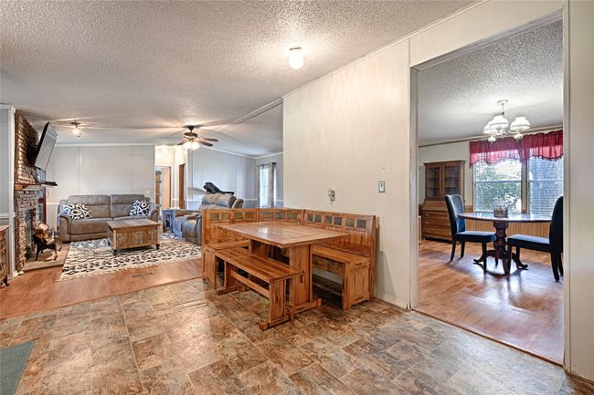 Eat in Kitchen overlloking the Living area with a brick fireplace, a textured ceiling, crown molding, and light stone finish flooring | Image 7
