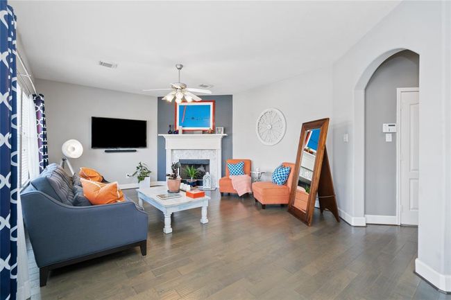 Bright and inviting living room featuring hardwood floors, a cozy fireplace, and a modern ceiling fan. The space is furnished with a comfortable sofa and vibrant chairs, complemented by stylish decor and plentiful natural light. | Image 13