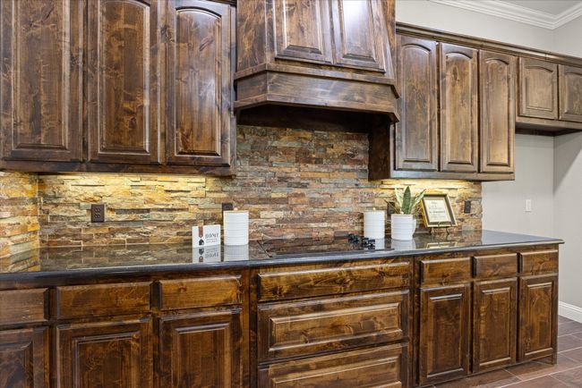Kitchen featuring backsplash, dark brown cabinetry, crown molding, and custom exhaust hood | Image 19