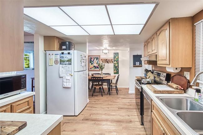 Kitchen with stainless steel appliances, light countertops, light brown cabinetry, light wood-style floors, and under cabinet range hood | Image 15